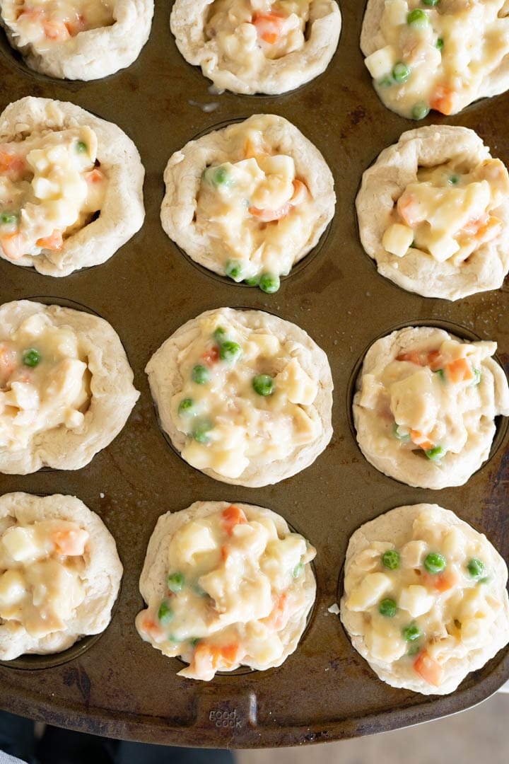 Raw biscuit chicken pot pies in a muffin tin prior to being baked. 