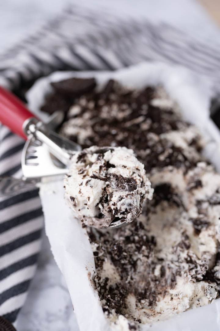 A container with homemade oreo ice cream with an ice cream scoop sitting on top. 