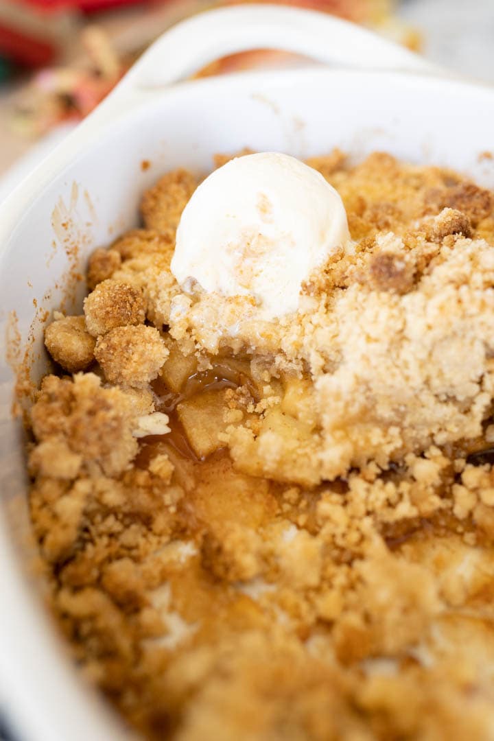 Baking dish filled with apple crisp with one scoop of vanilla ice cream in the corner. 