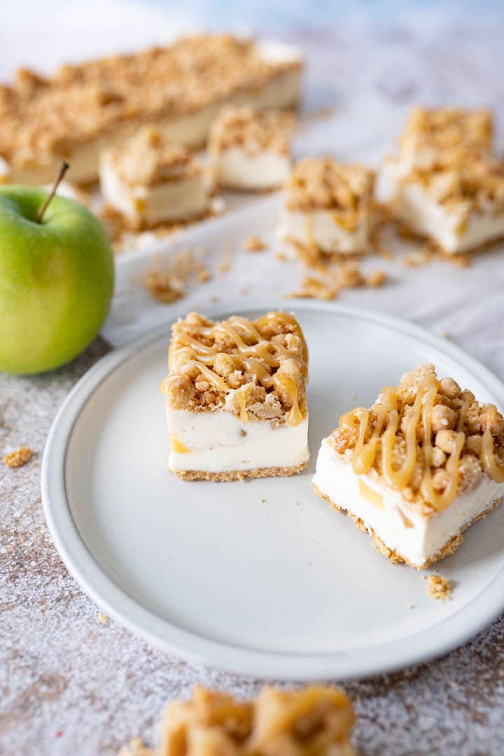 Side view of 2 apple pie cheesecake bars on a plate on the counter.