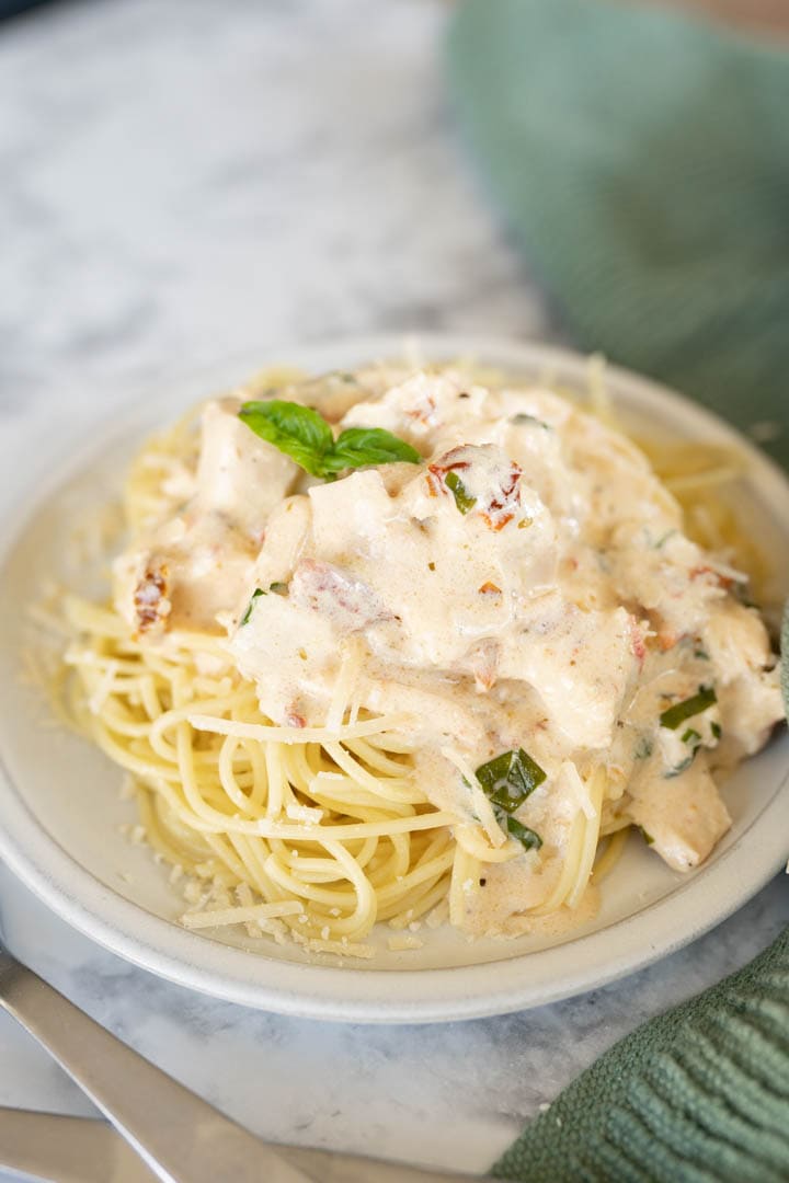 A close up of a plate of marry me chicken served over pasta and topped with basil.