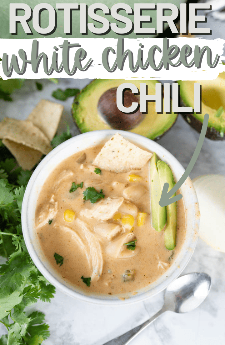 A bowl of white chicken chili on the counter surrounded by cilantro and avocados.