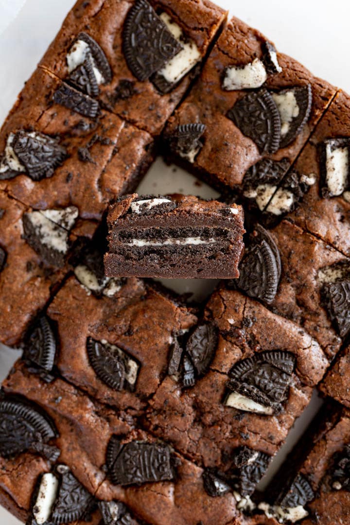 A close up of a tray of oreo brownies. One brownie is cut out of the middle and turned up.