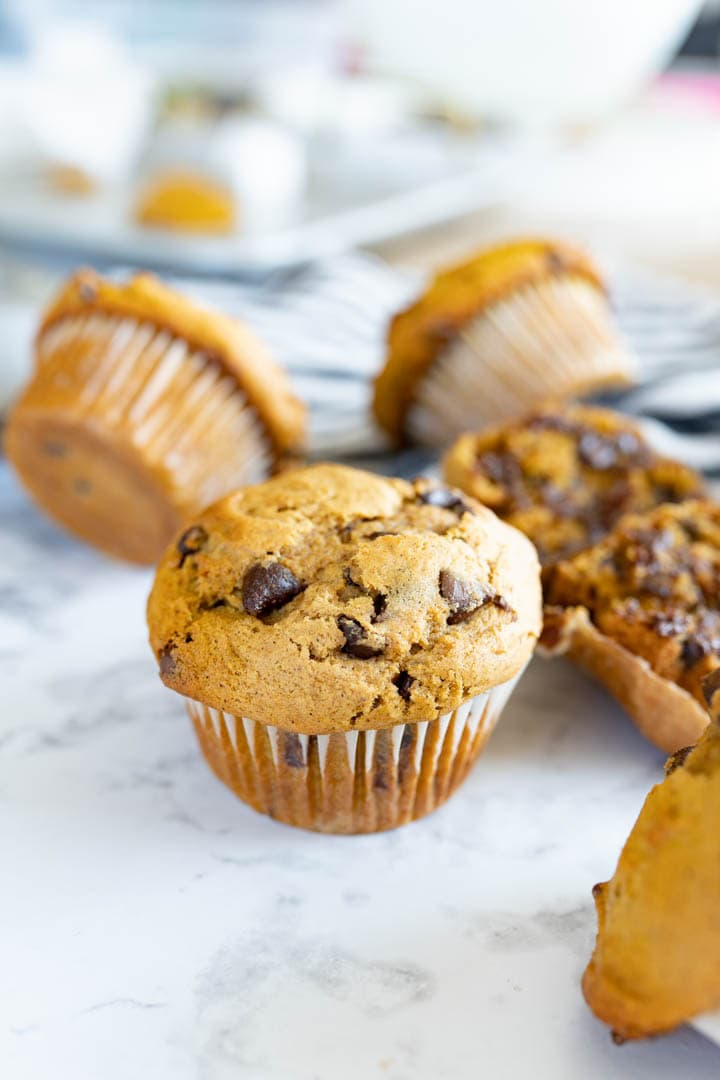 A countertop filled with pumpkin chocolate chip muffins. Some are turned on their side and others have been opened to show the gooey chocolate chips.