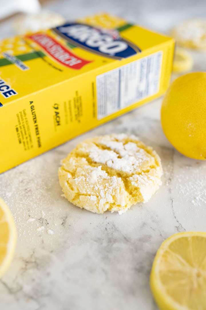 lemon crinkle cookie on the counter next to a lemon and a yellow box of Argo corn starch. 