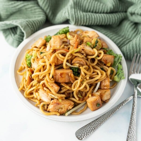 A bowl filled with chicken chow mein on top of a green towel.