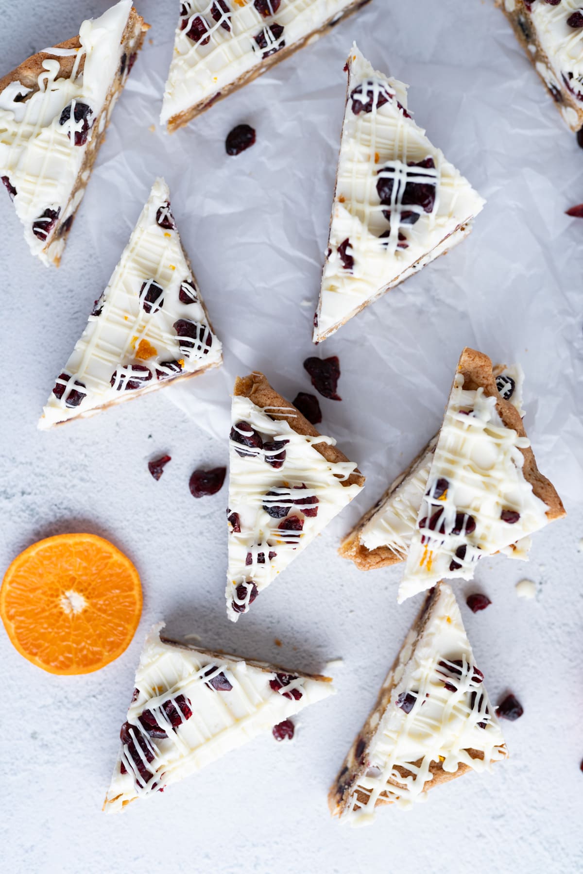 Aerial view of copycat starbucks cranberry bliss bars cut into triangles and scattered on the counter with an orange slice. 