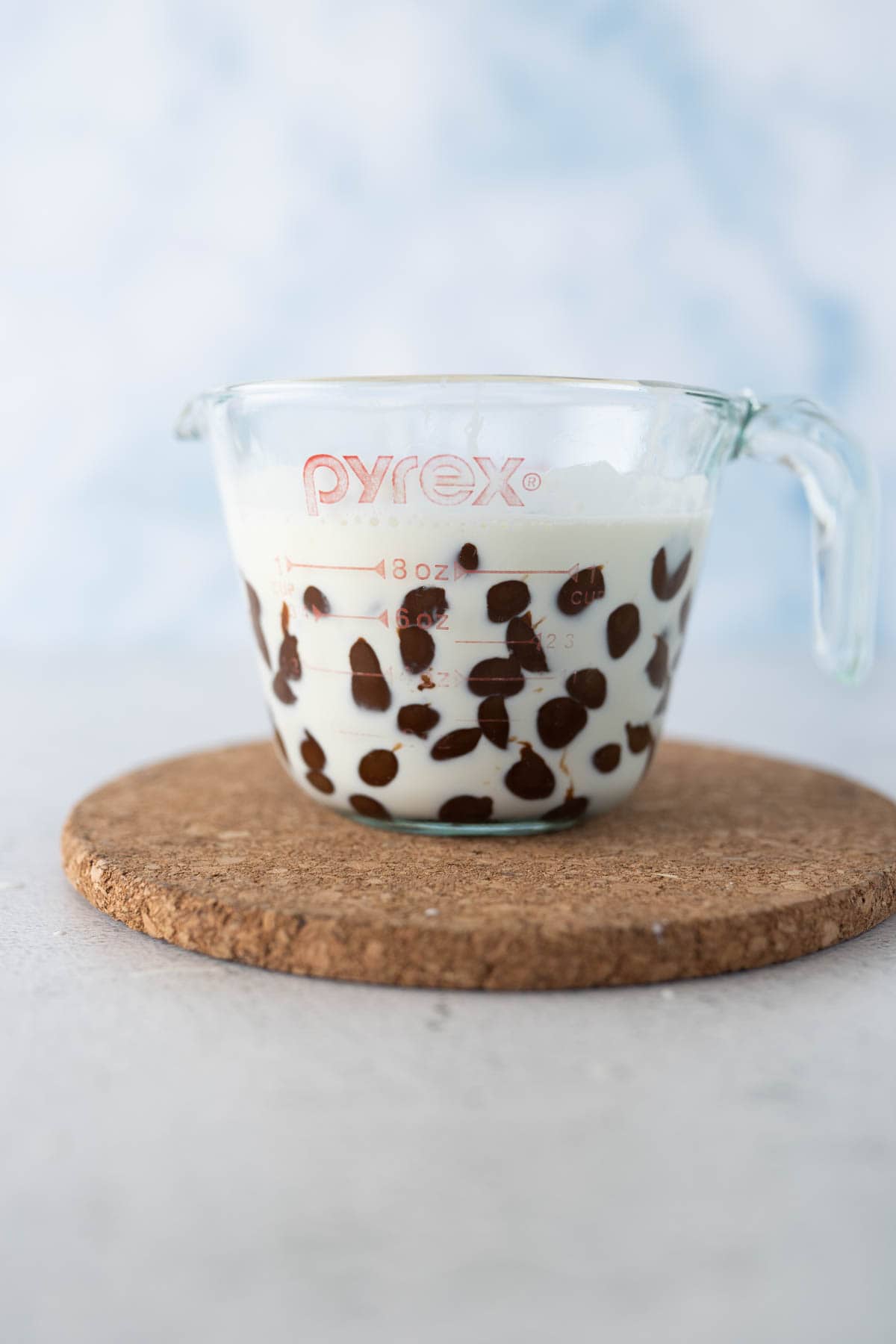 A measuring cup of hot heavy cream with chocolate chips in it resting to make the chocolate ganche. 