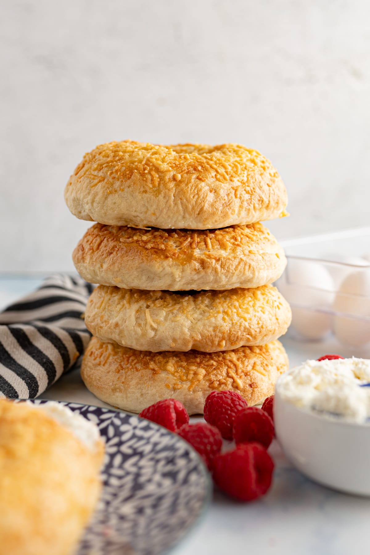 asiago bagels stacked on top of each other with some raspberries and cream cheese next to it. 