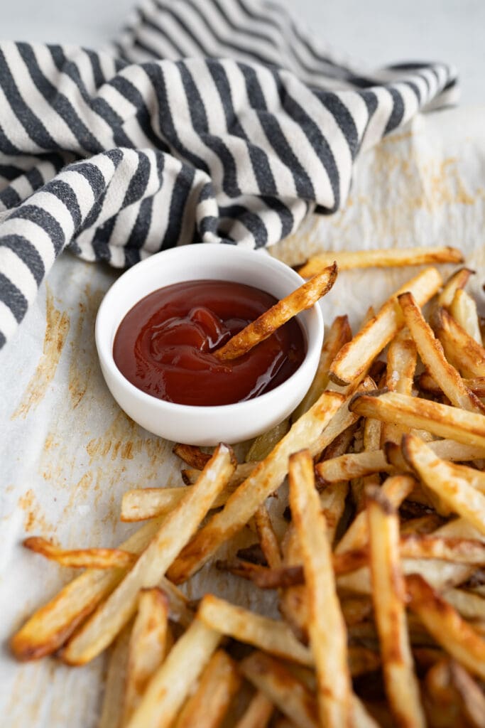 Crispy homemade french fries being dipped into a bowl of ketchup. 
