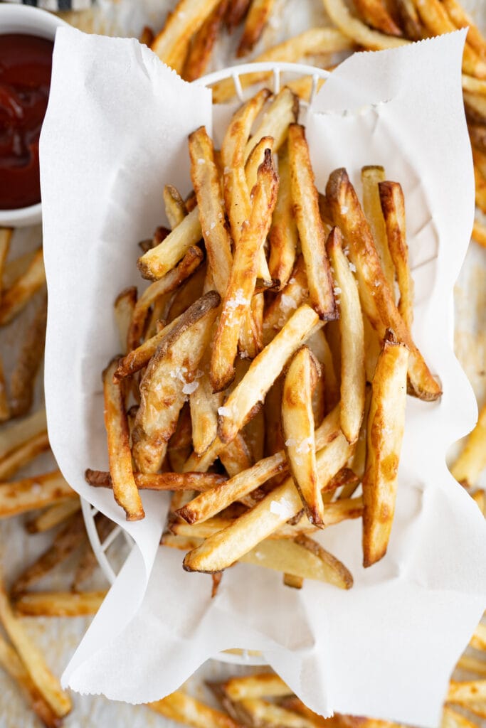 A serving of homemade french fries on a piece of parchment paper on top of additional fries.
