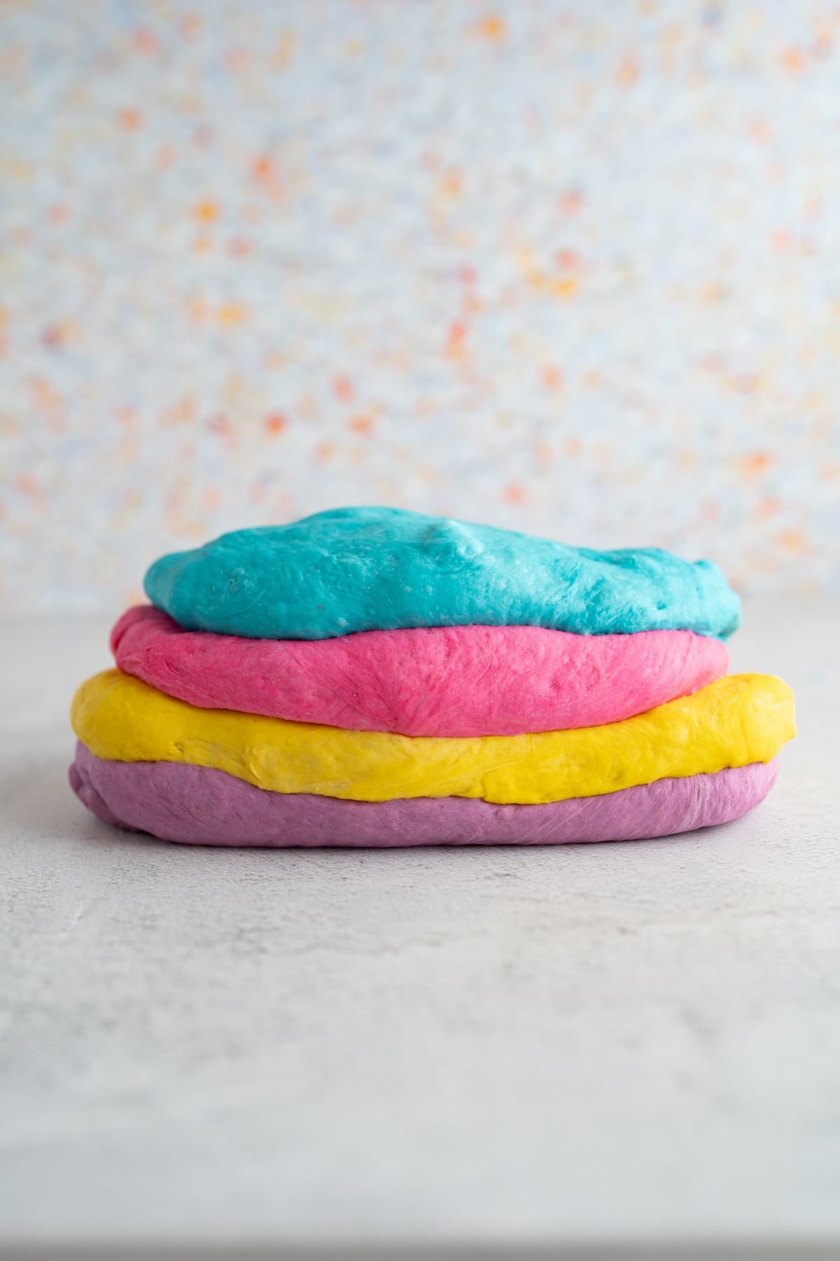Four different colors of dough stacked on top of each other for homemade rainbow bagels. 