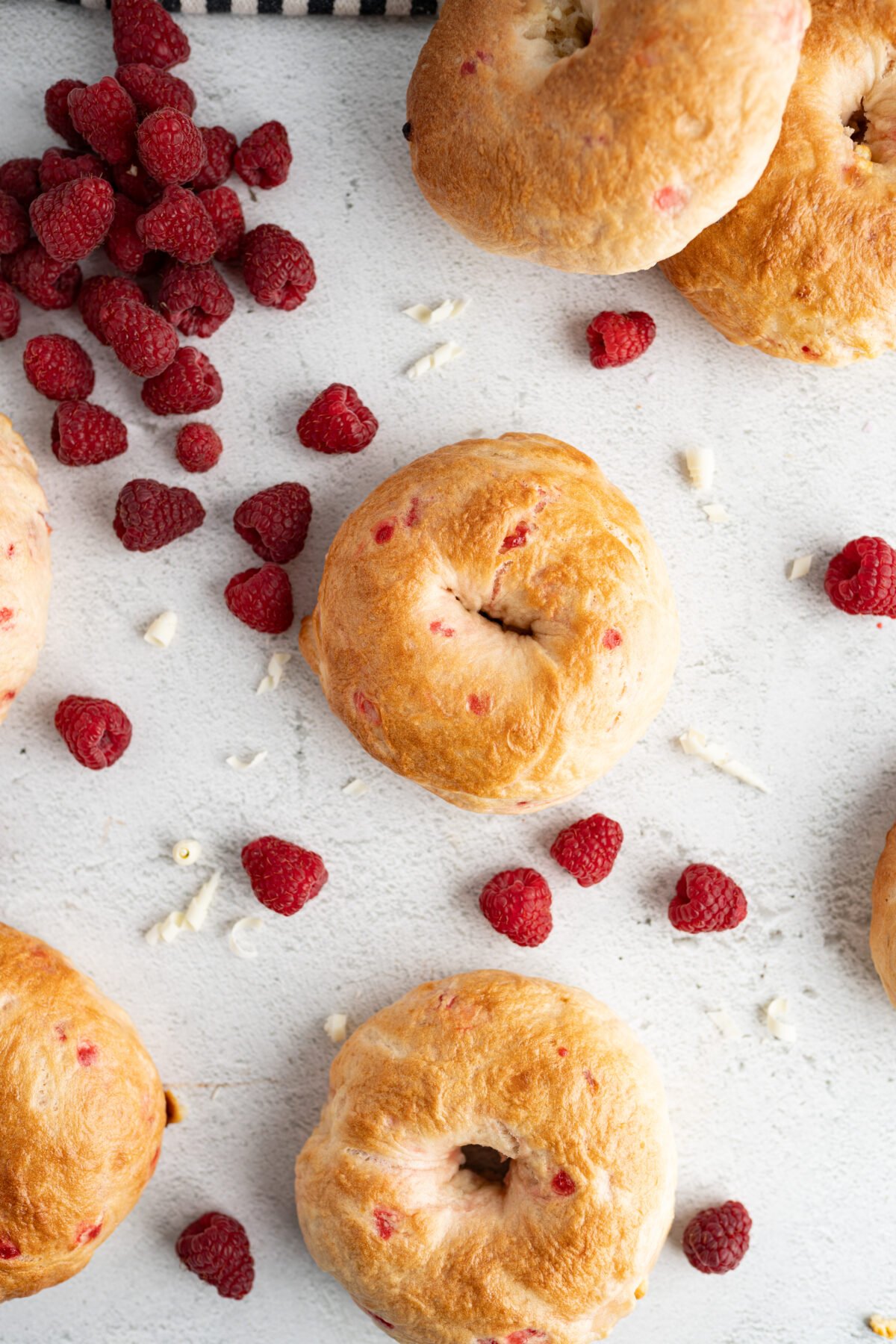 Aerial view of homemade bagels on the counter scattered with raspberries. 