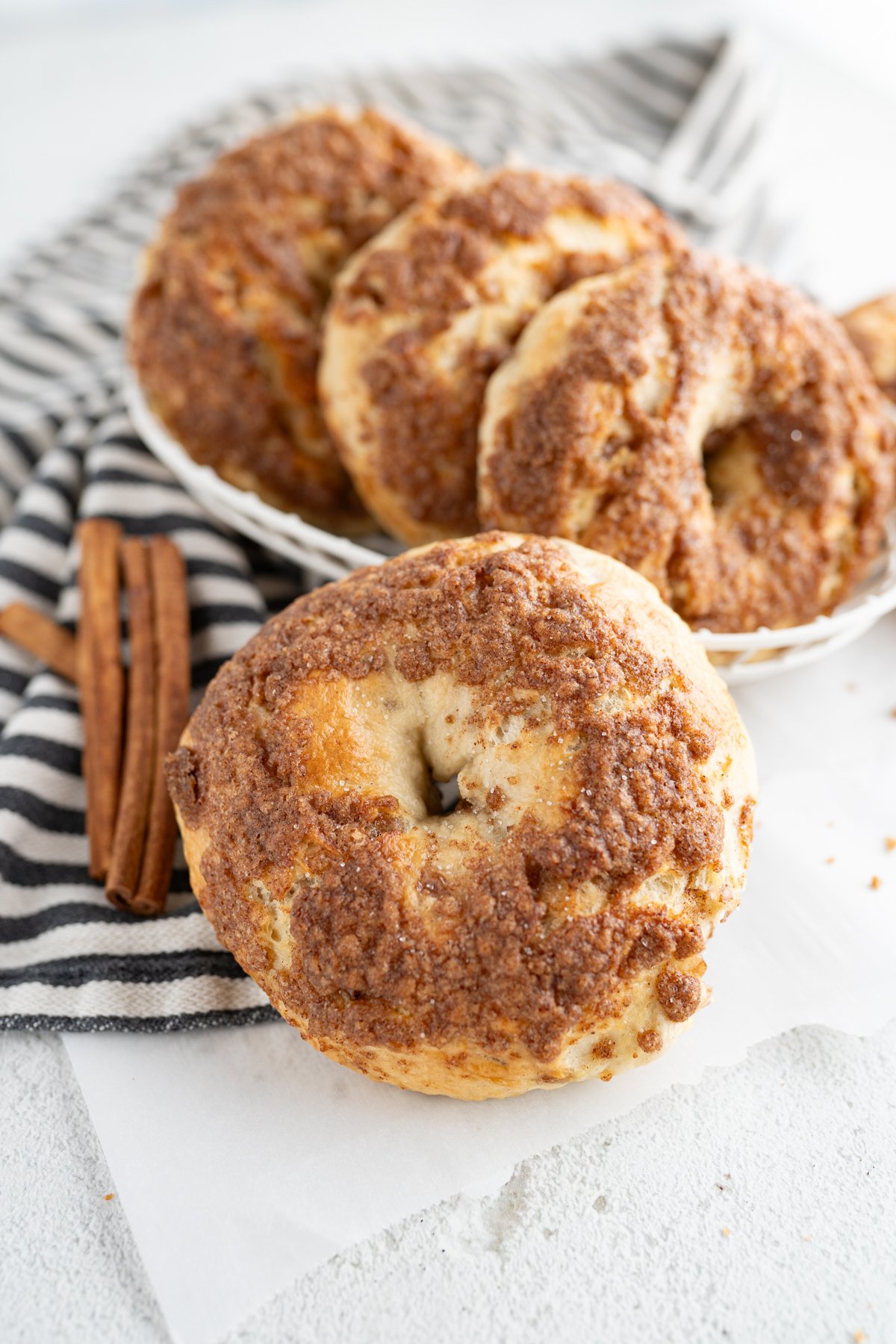 A bowl of cinnamon crunch bagels on the counter next to cinnamon sticks. 
