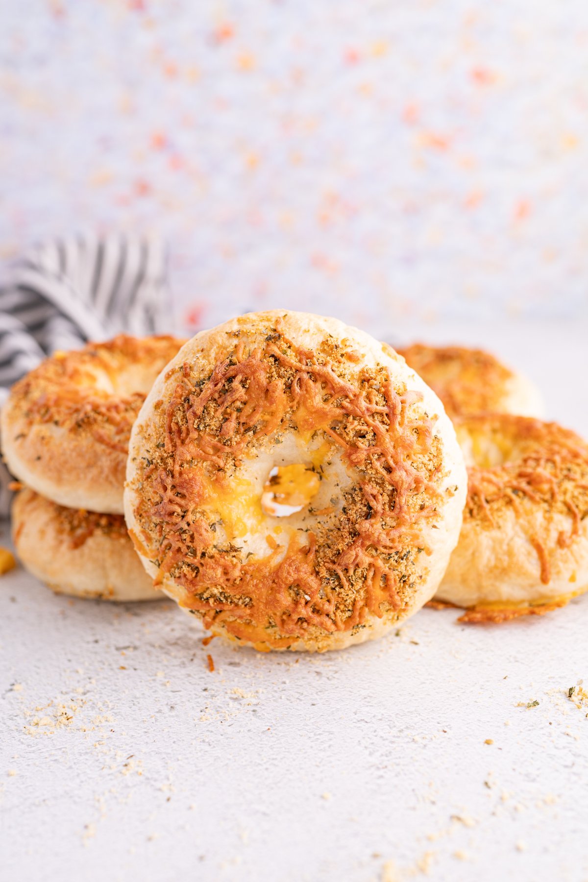 An italian herb and cheese bagel stacked in front of a pile of bagels. 