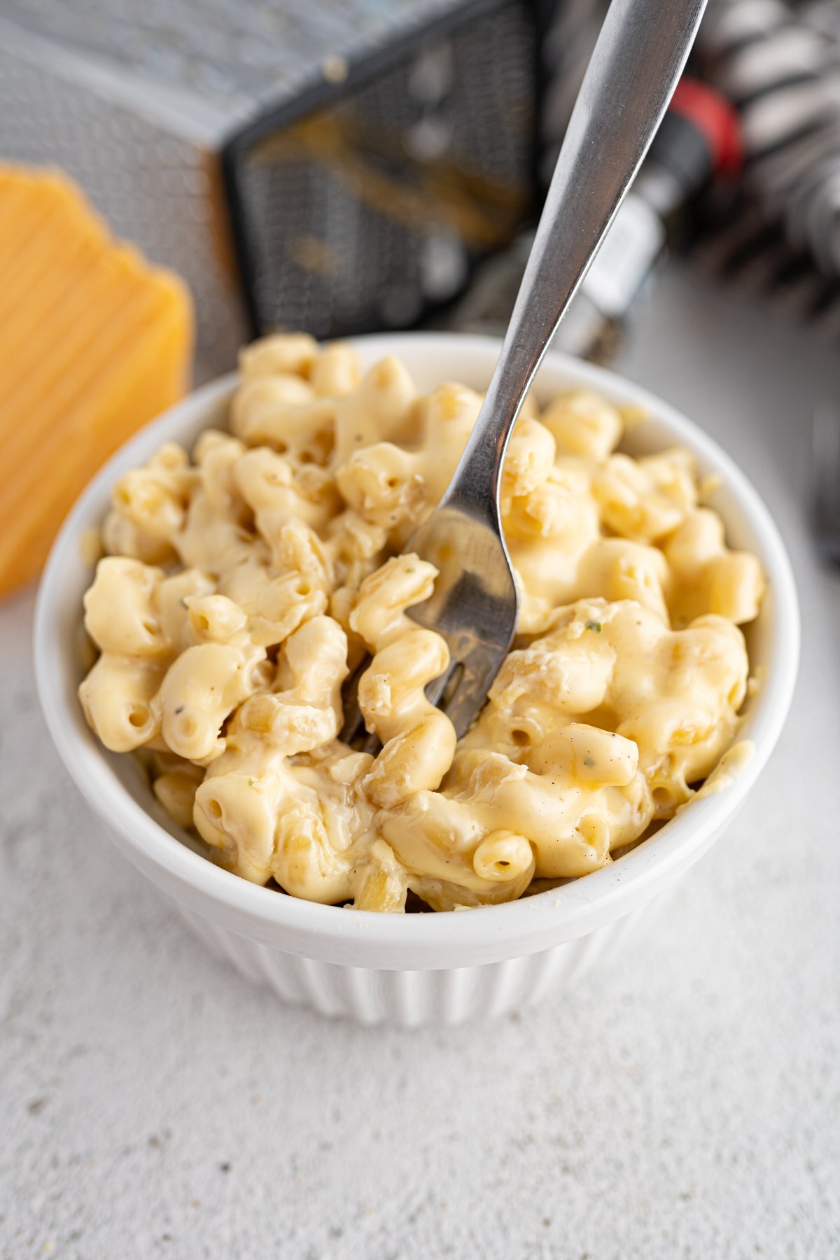 A fork scooping a bite of baked mac n cheese out of a bowl. 