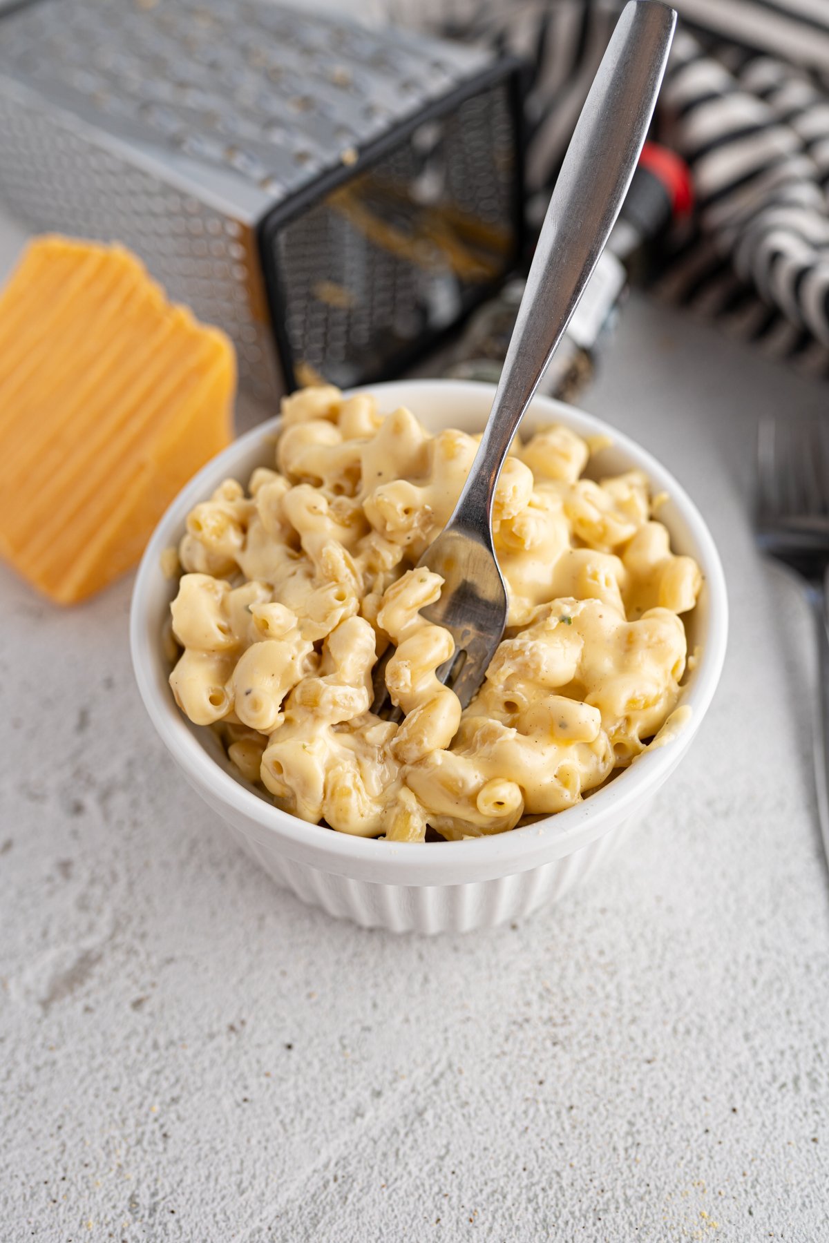 A fork scooping a bite of baked mac n cheese out of a bowl.