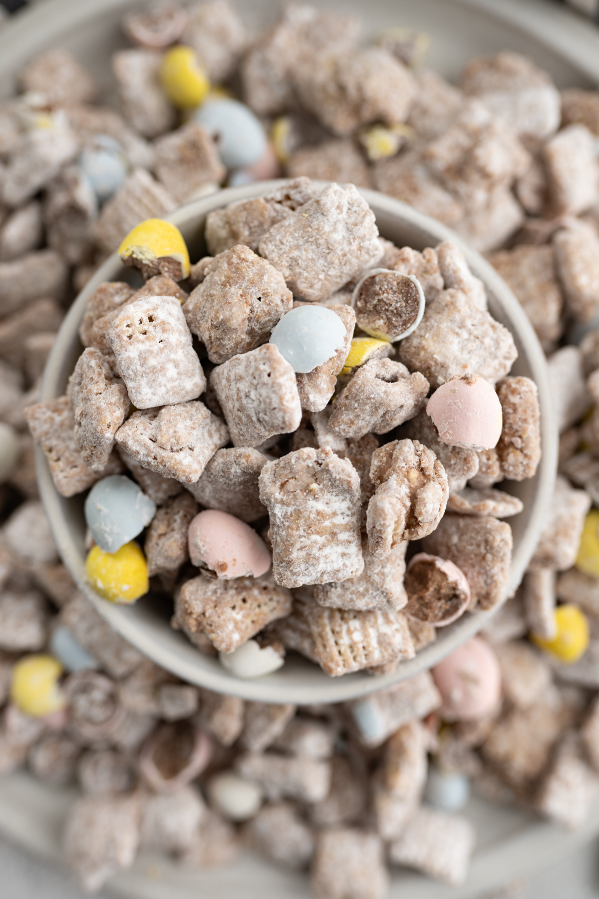 Aerial view of easter muddy buddies in a bowl overflowing onto a plate. 