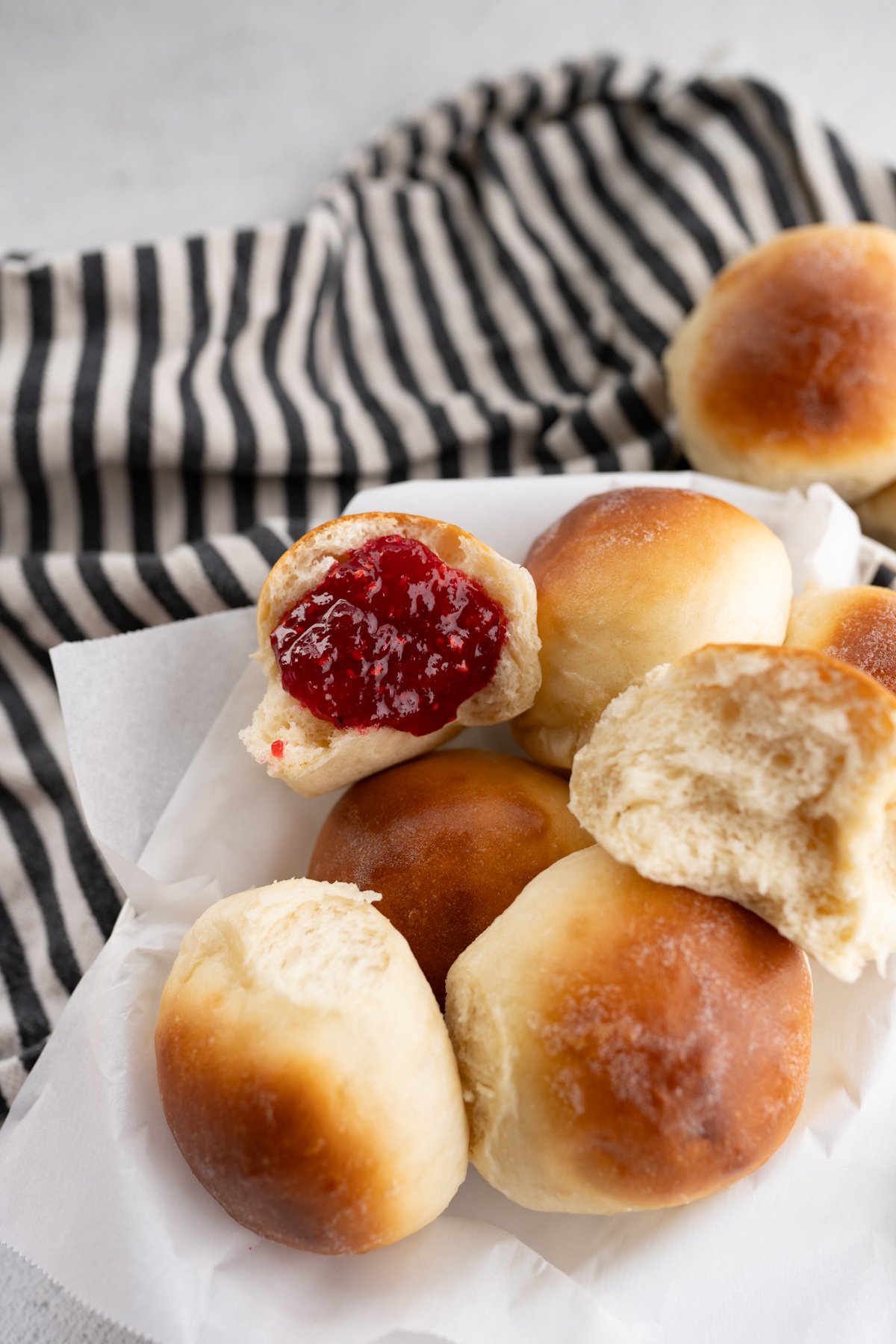 A pile of homemade rolls. One is cut open with raspberry jam inside. 