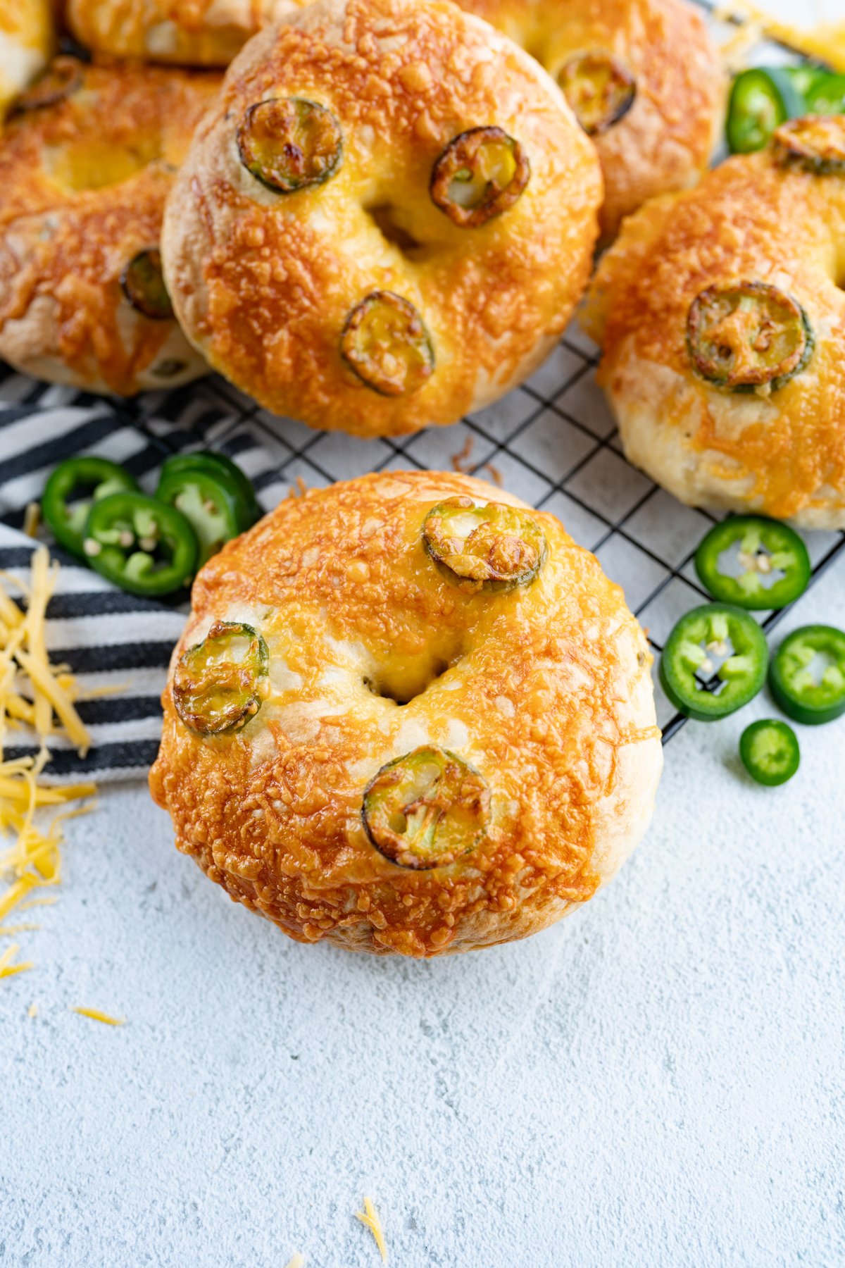 a jalapeno cheddar bagle on a counter top next to some sliced jalapeños. 