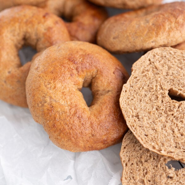 A pile of wheat bagels on the counter. One is cut in half.
