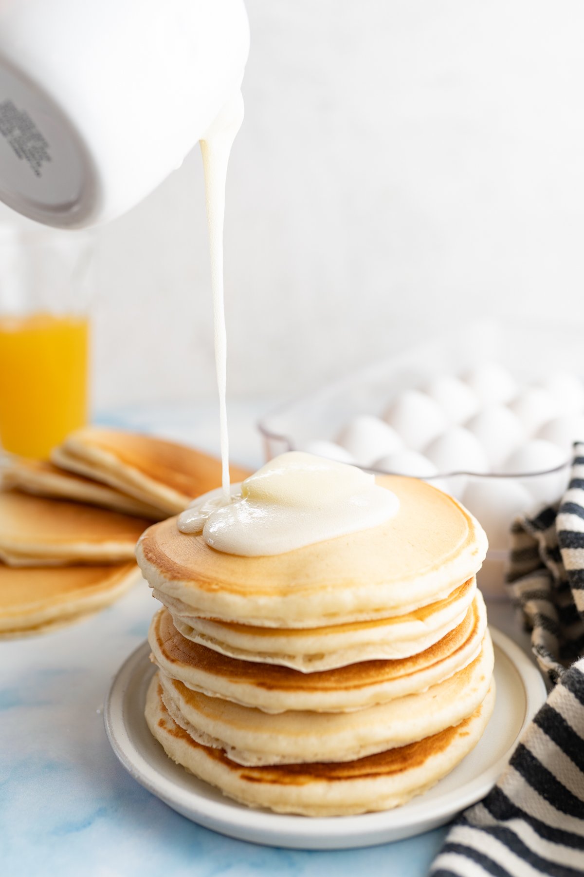 A carafe of homemade buttermilk syrup being drizzled on top of a stack of pancakes. 