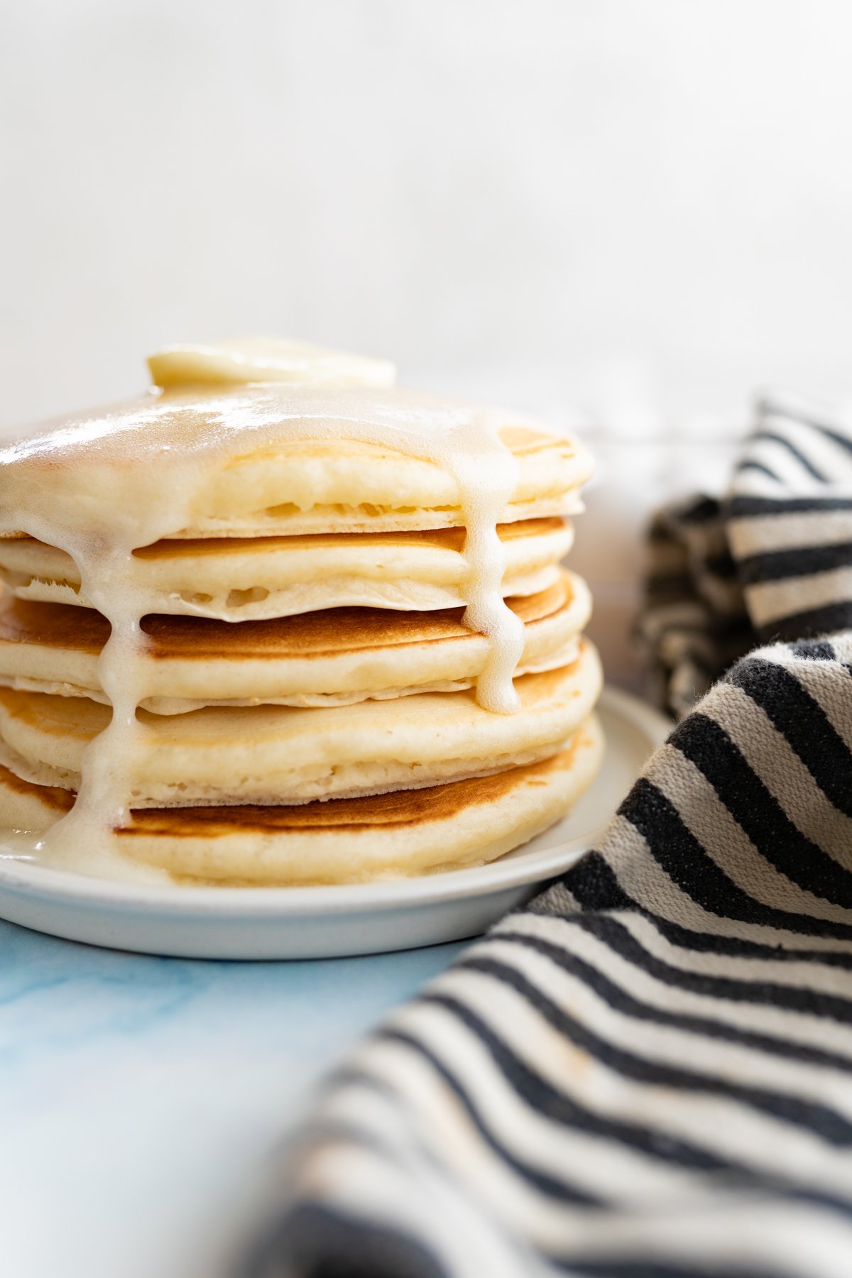 Side view of a stack of pancakes that have buttermilk syrup dripping down the sides. 