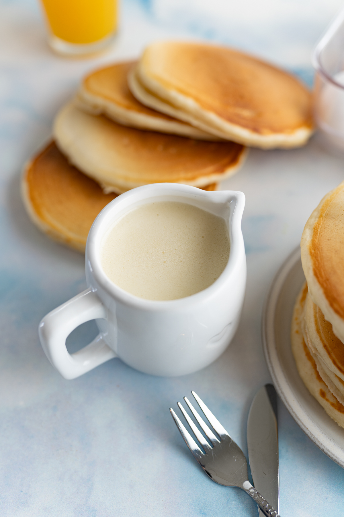 Aerial view of a counter top with pancakes fanned out next to a small carafe of buttermilk syrup. 