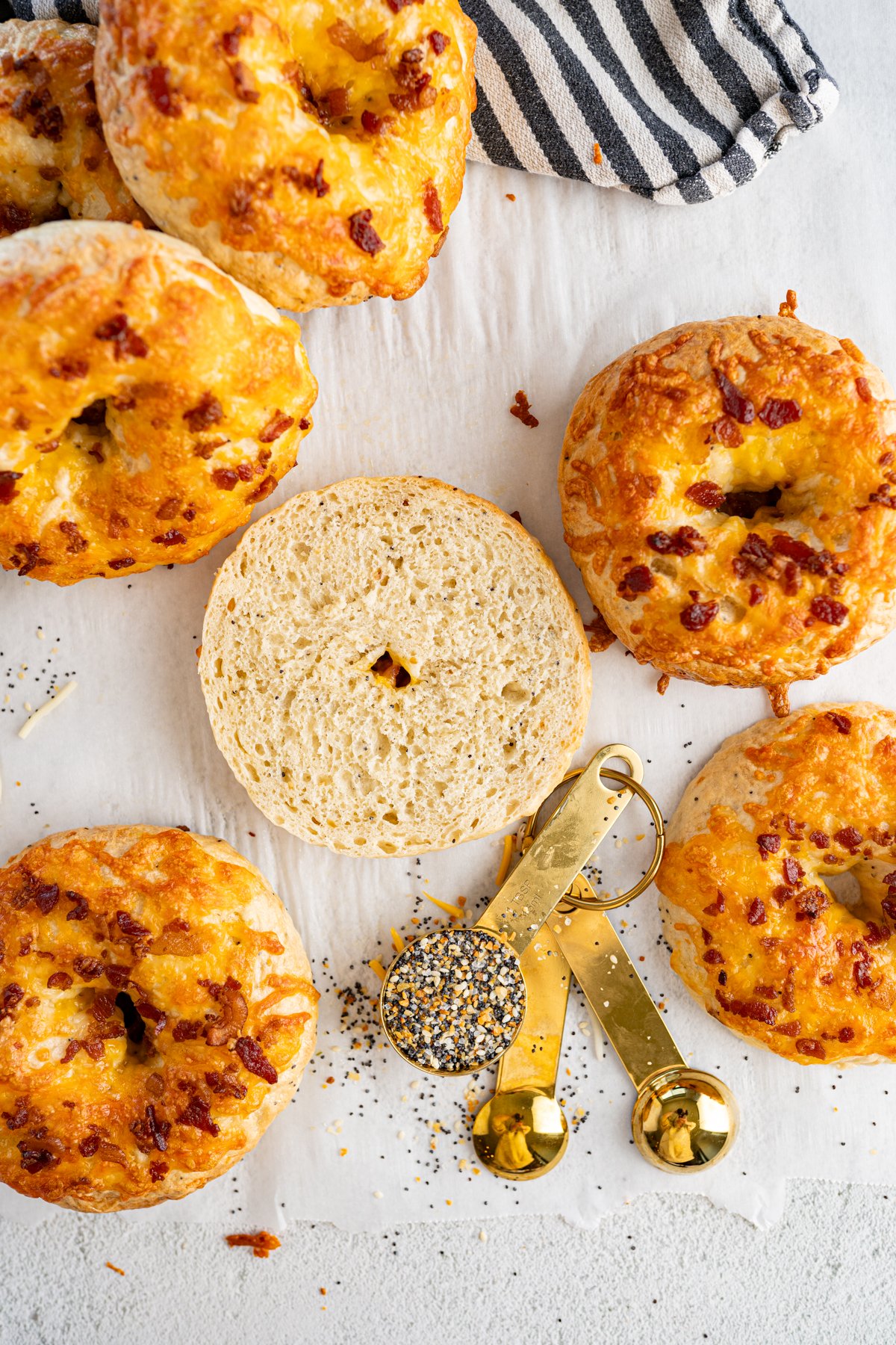 Homemade everything bagels topped with cheddar and bacon. One is sliced in half, exposing the inside. 