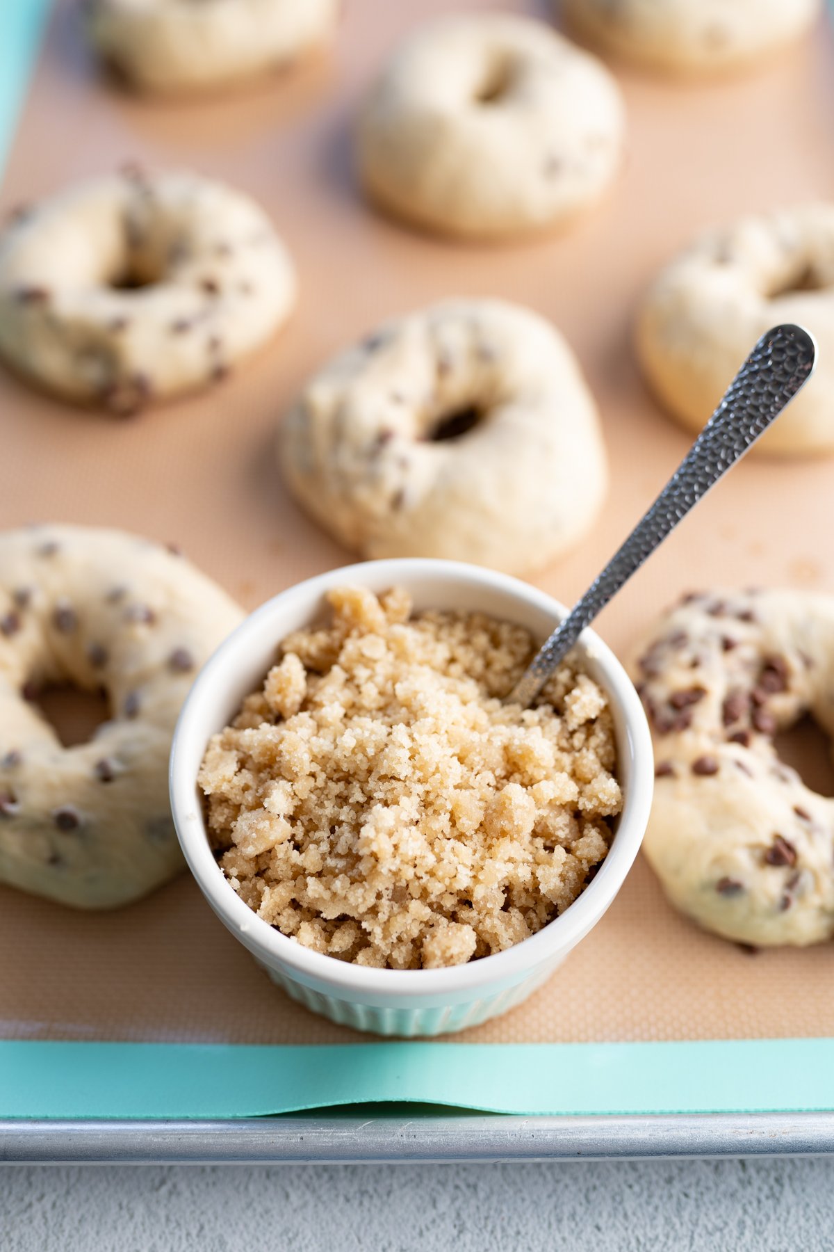 Unbaked cookie dough bagels next to a bowl of cookie dough crunch topping. 