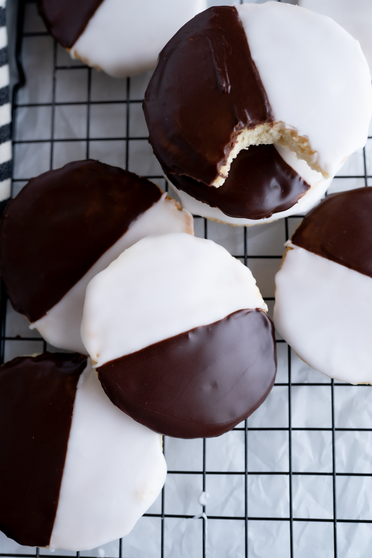 Aerial view of a cooling rack filled with black and white cookies. One cookie has a bite taken out of it. 