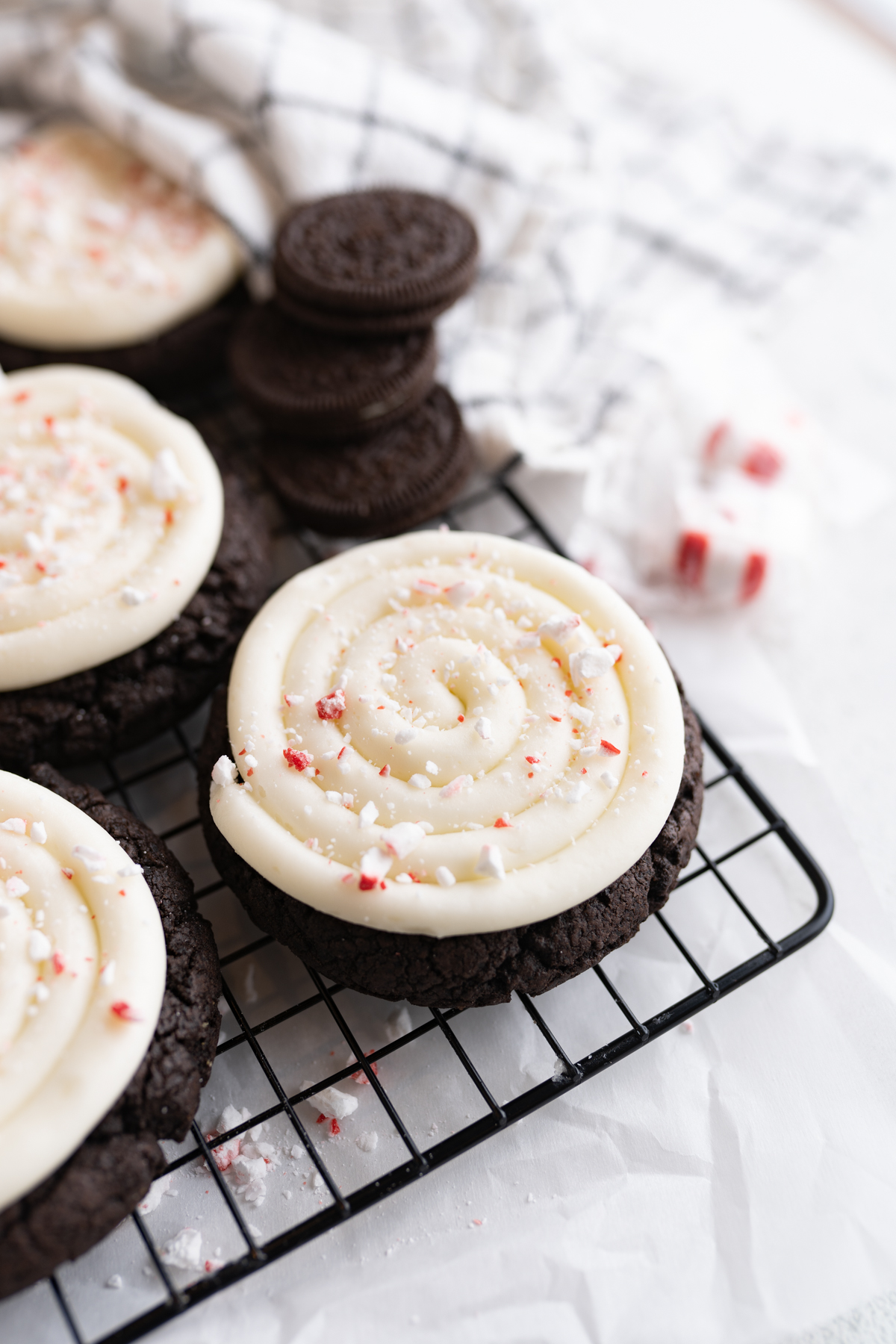 Close up of a chocolate oreo cookie topped with frosting and peppermint candies. 