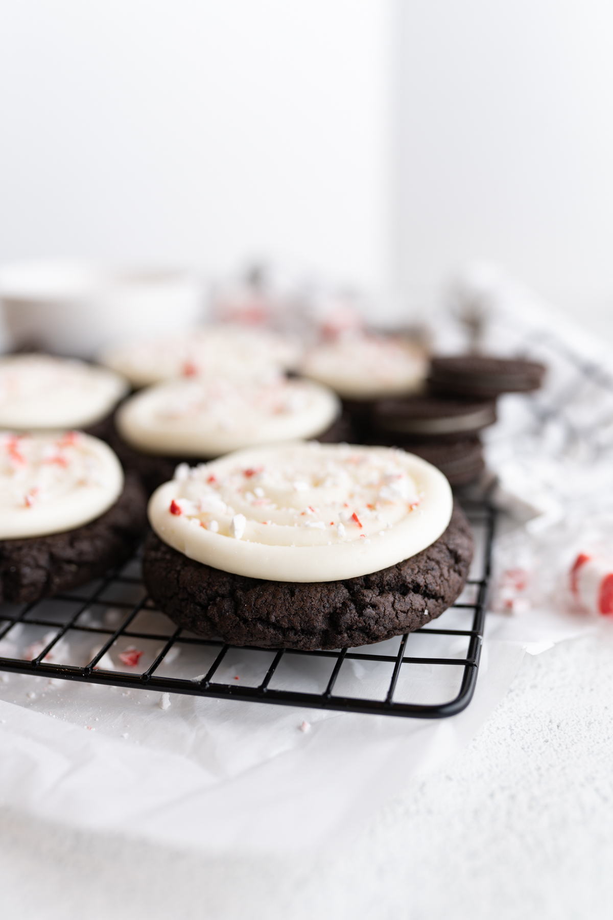 Side view of giant chocolate cookies stuffed with oreos and topped with cream cheese frosting and peppermint. 