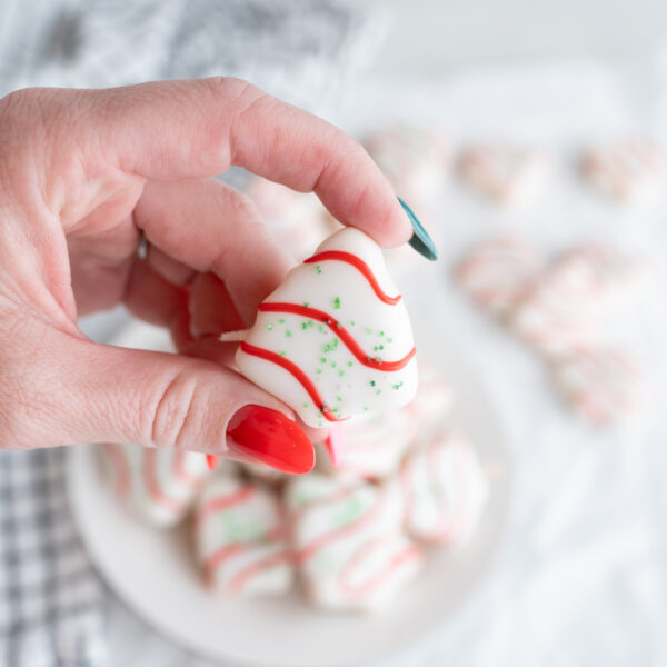 Close up of a hand holding a tiny sugar cookie decorated like Little Debbie's Christmas Trees.