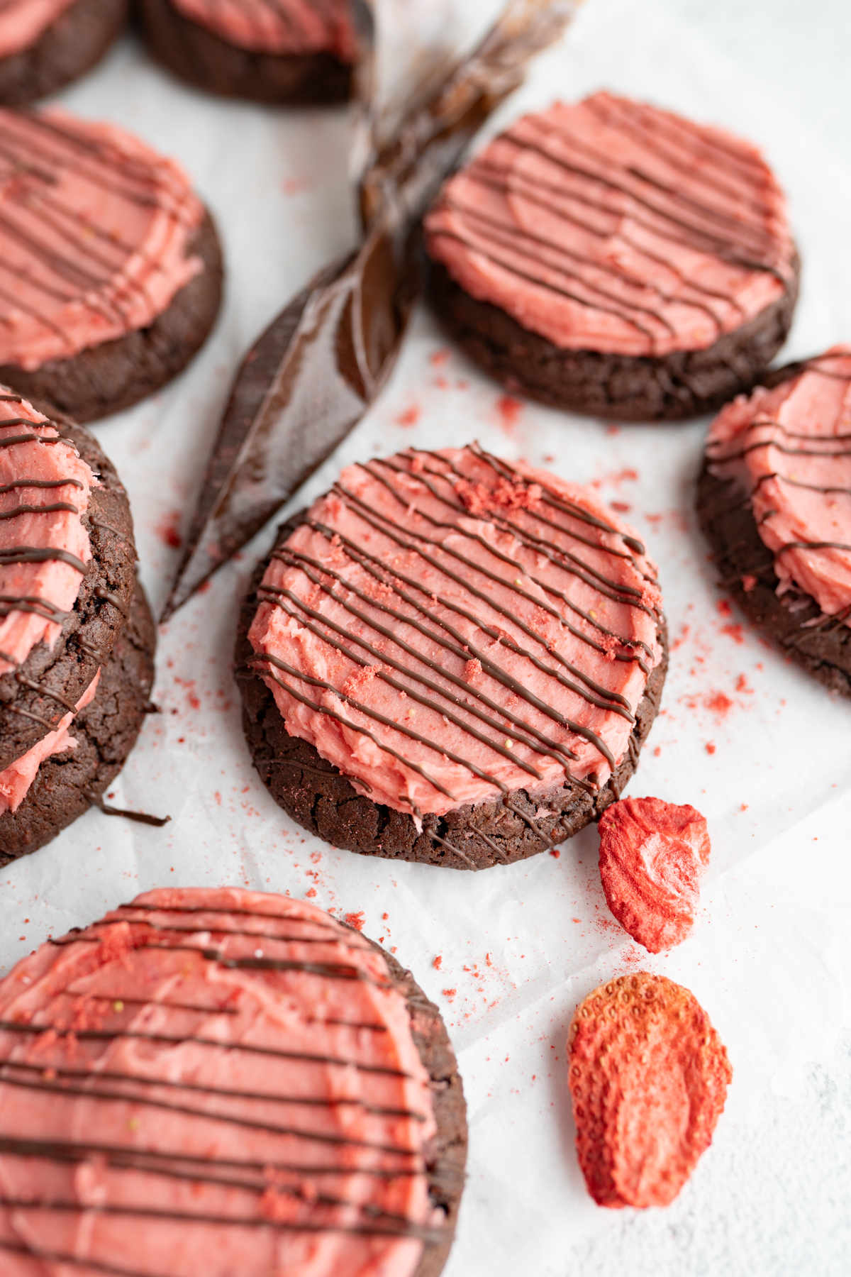 Close up of a chocolate strawberry cookie topped with strawberry buttercream and a chocolate drizzle. 