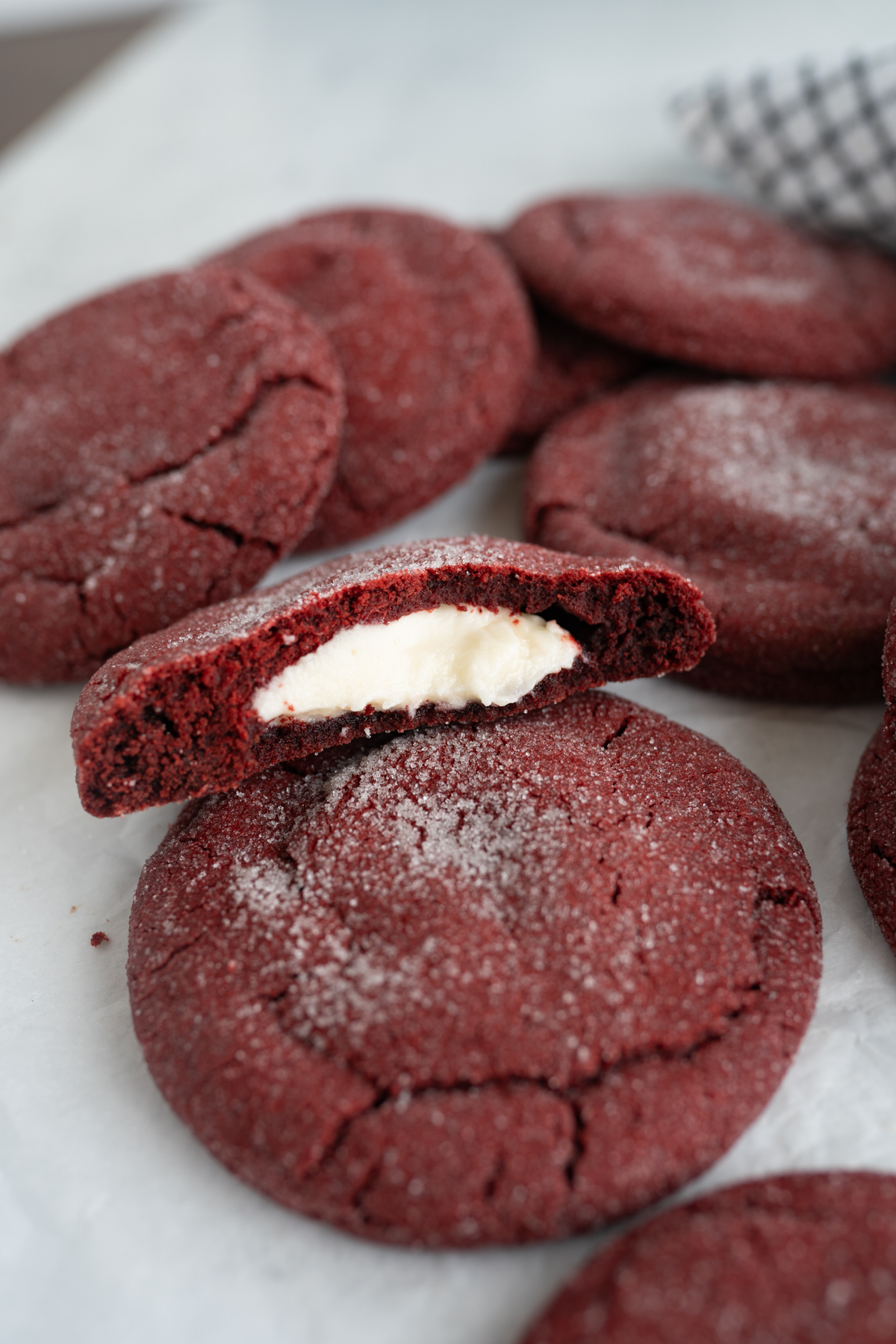 A red velvet cookie stuffed with a cream cheese frosting. One cookie is cut in half and propped on a full cookie.