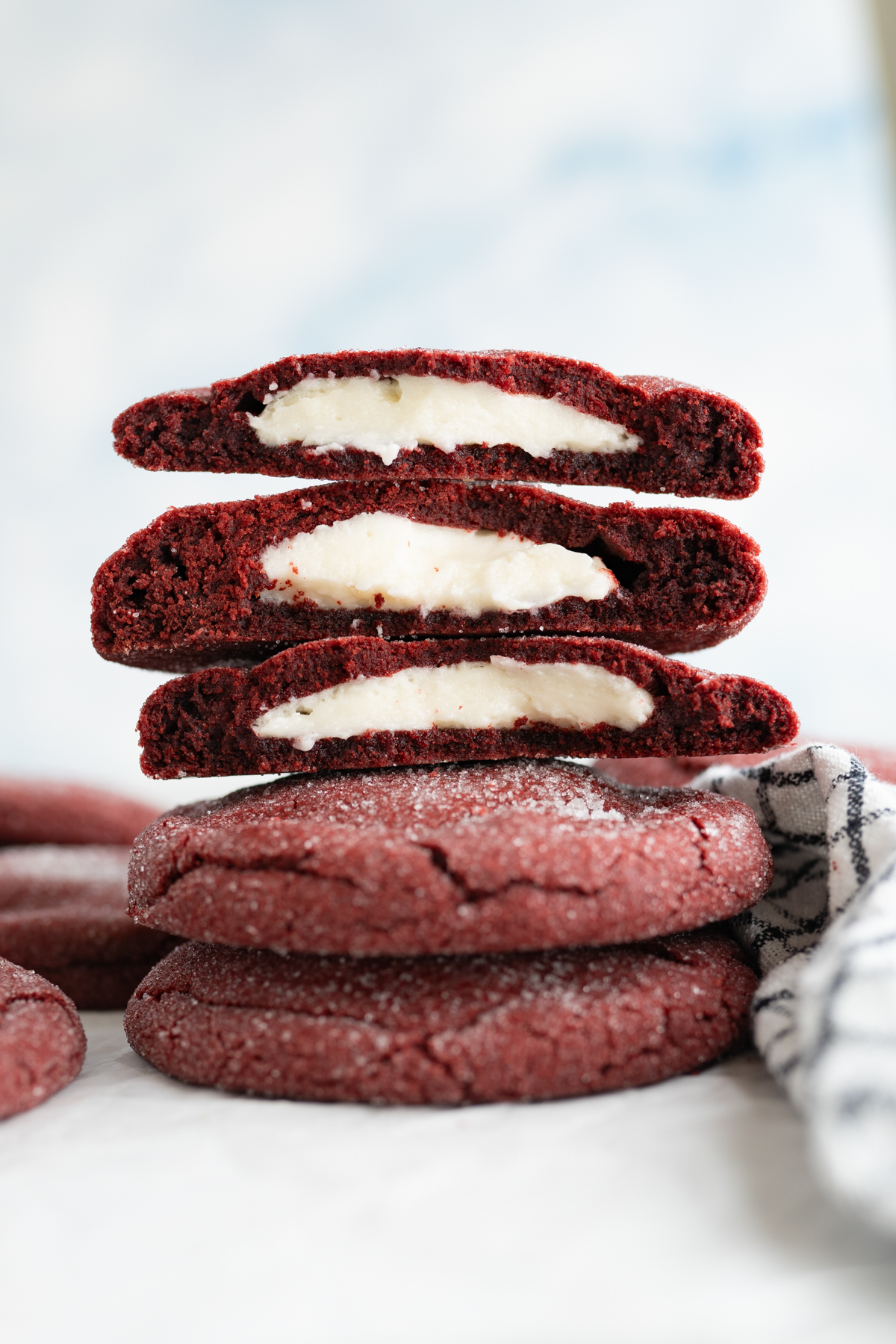 A stack of stuffed red velvet cookies, cut in half to reveal a cream cheese frosting inside.