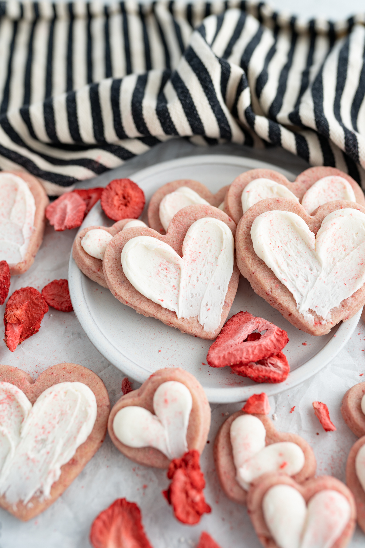 A plate of strawberry cut out sugar cookies topped with frosting. 
