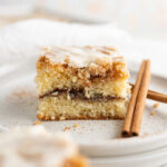 Close up of a square of coffee cake next to a cinnamon stick.