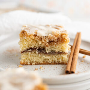 Close up of a square of coffee cake next to a cinnamon stick.