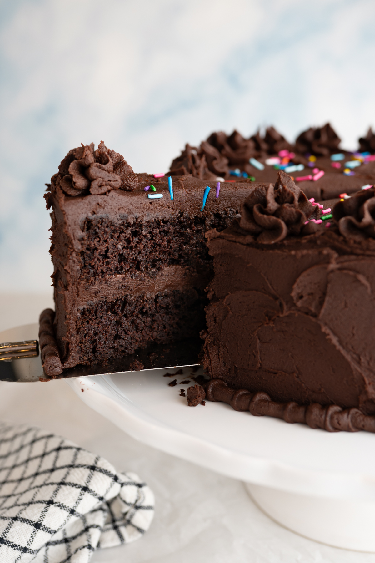 Side view of a chocolate cake with a slice being removed. 