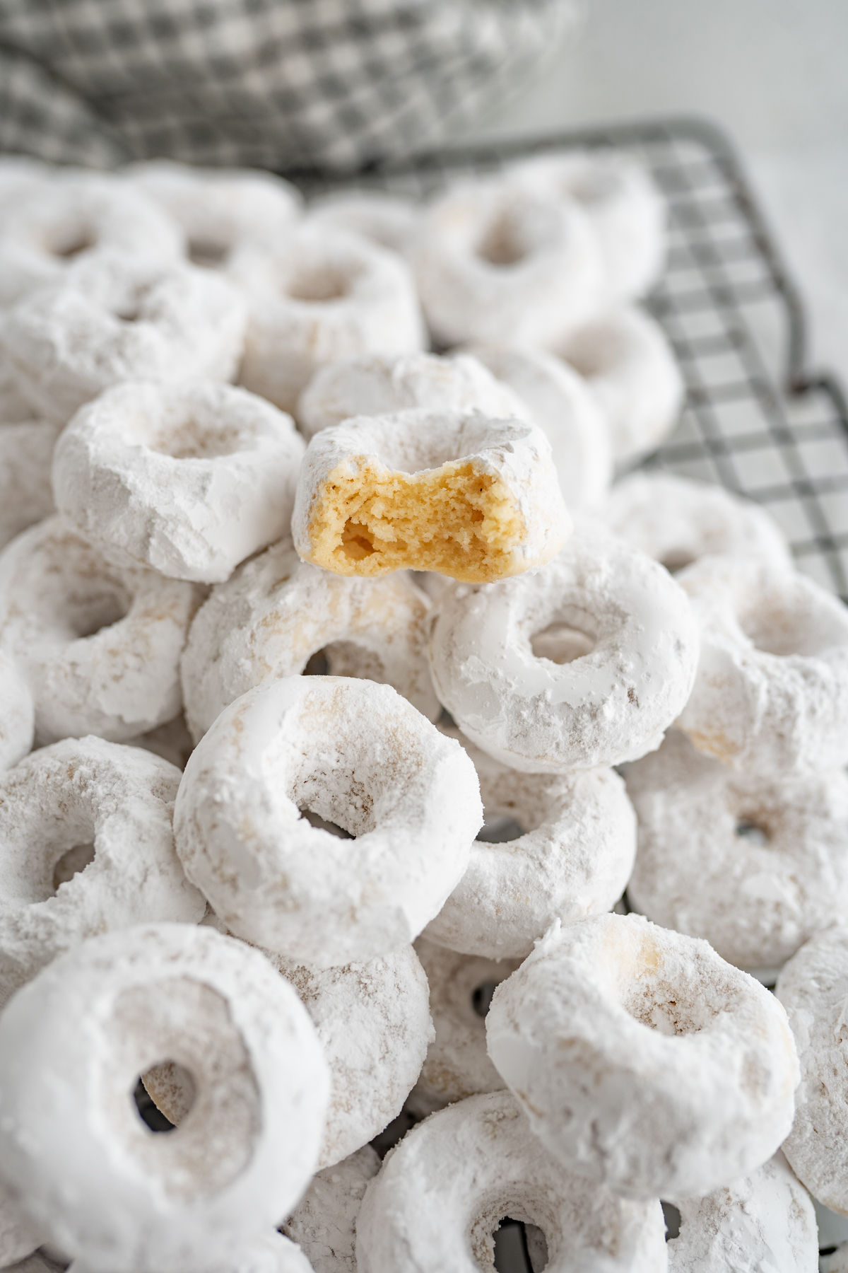 A pile of powdered mini donuts. On top one has a bite out of it. 